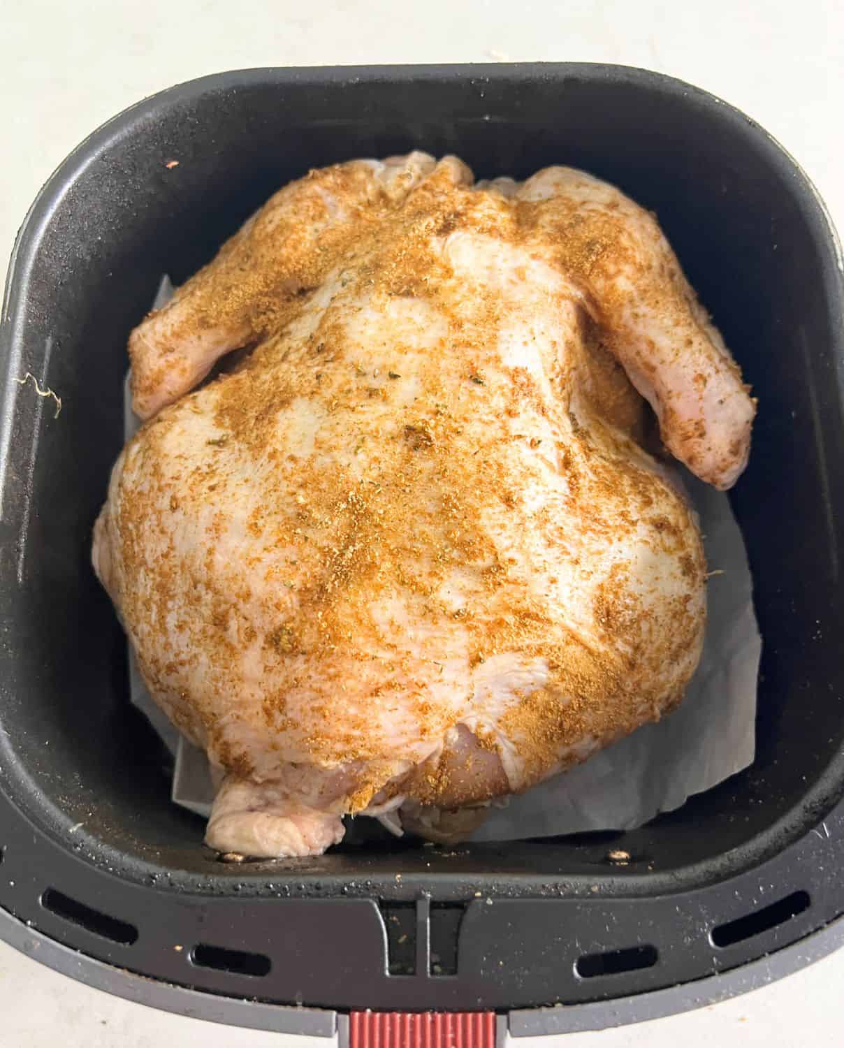 Seasoned whole chicken in air fryer basket. 