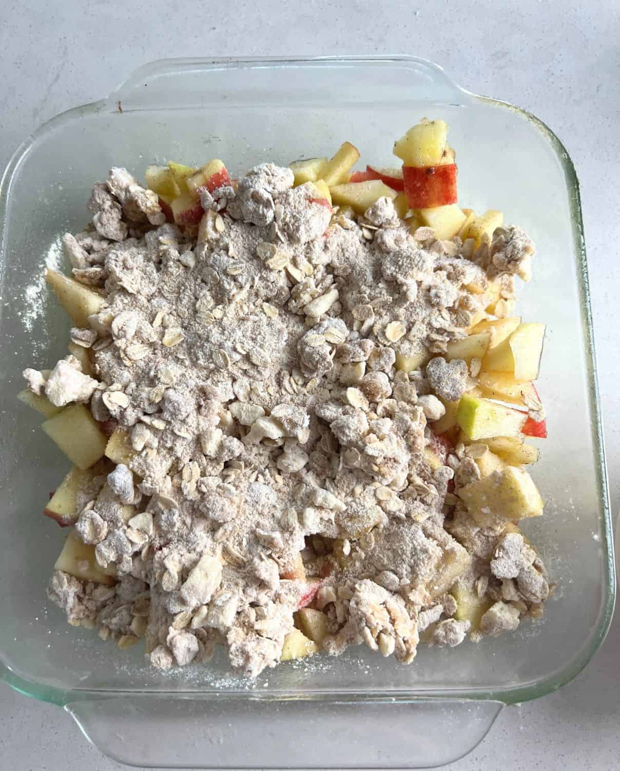 Crumble topping on top of apples in a baking dish. 