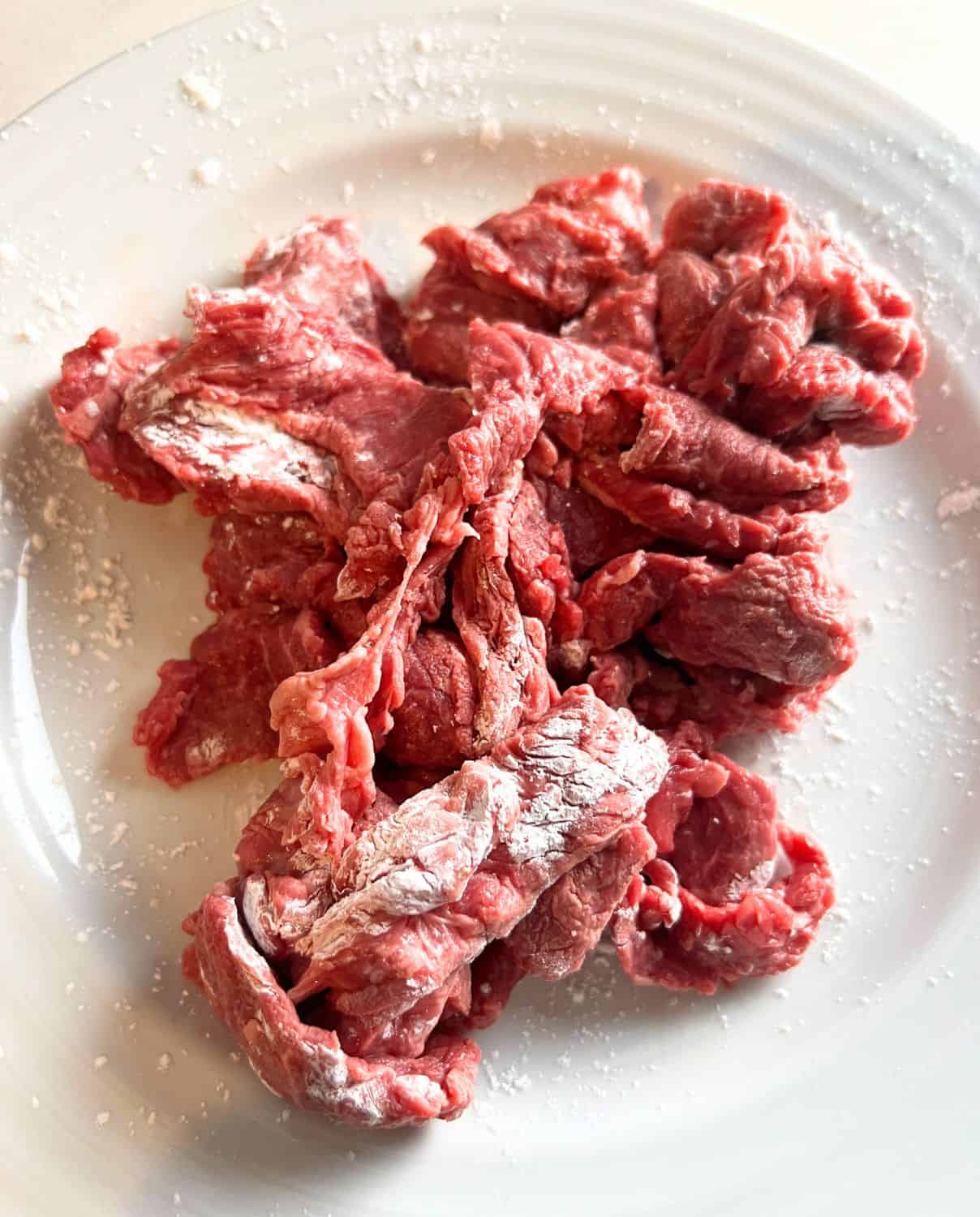 Beef mixed together with cornstarch on a plate. 