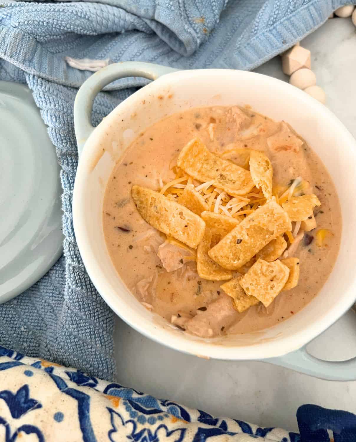 Chicken tortilla soup in a white serving dish topped with chips and cheese. 