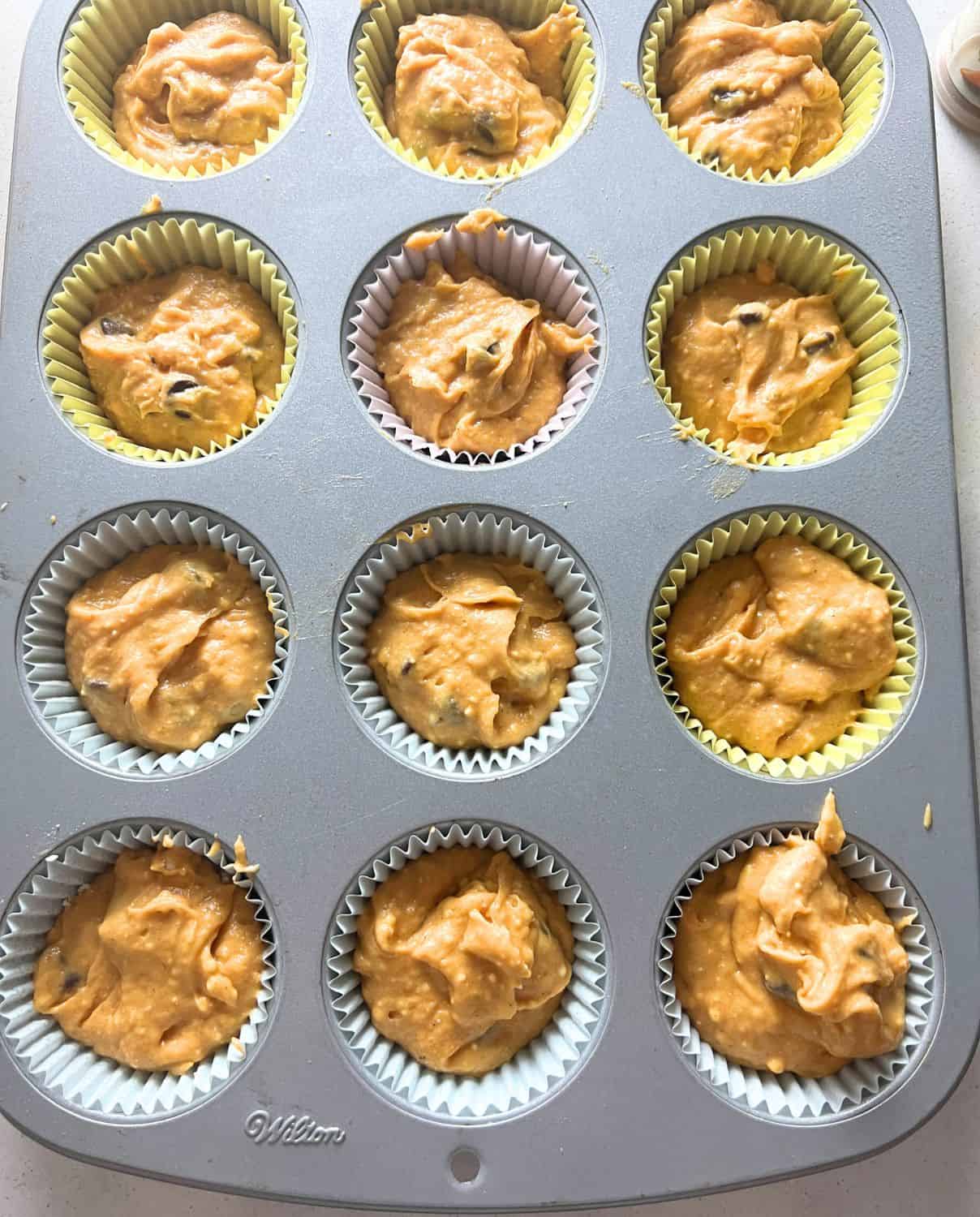 Pumpkin muffin batter scooped into muffin tin liners. 