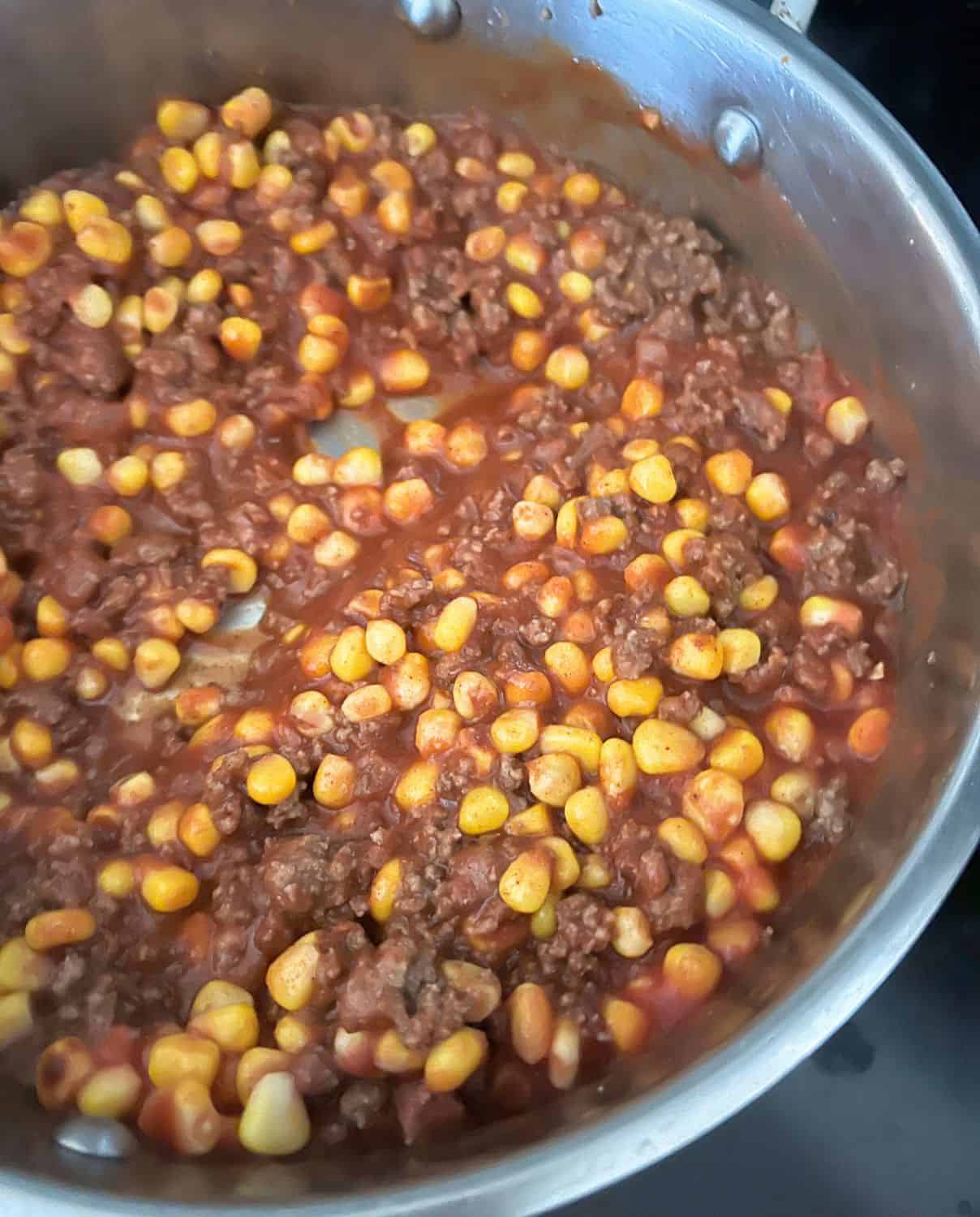 Ground beef mixed with corn and taco seasonings in a skillet. 