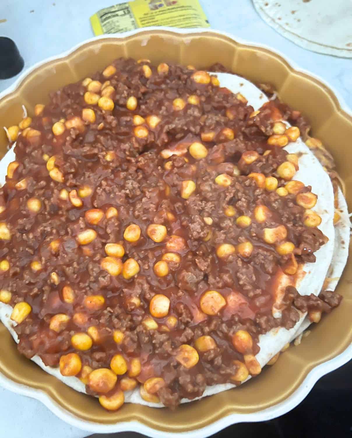 Beef and Corn mixture topped with tortillas in a casserole dish. 