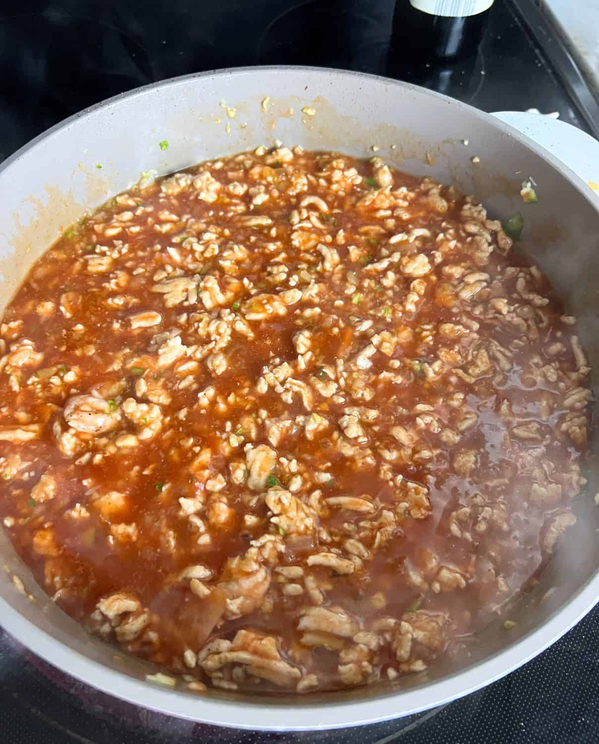 Enchilada sauce, ground turkey, and vegetables simmering in a pan. 