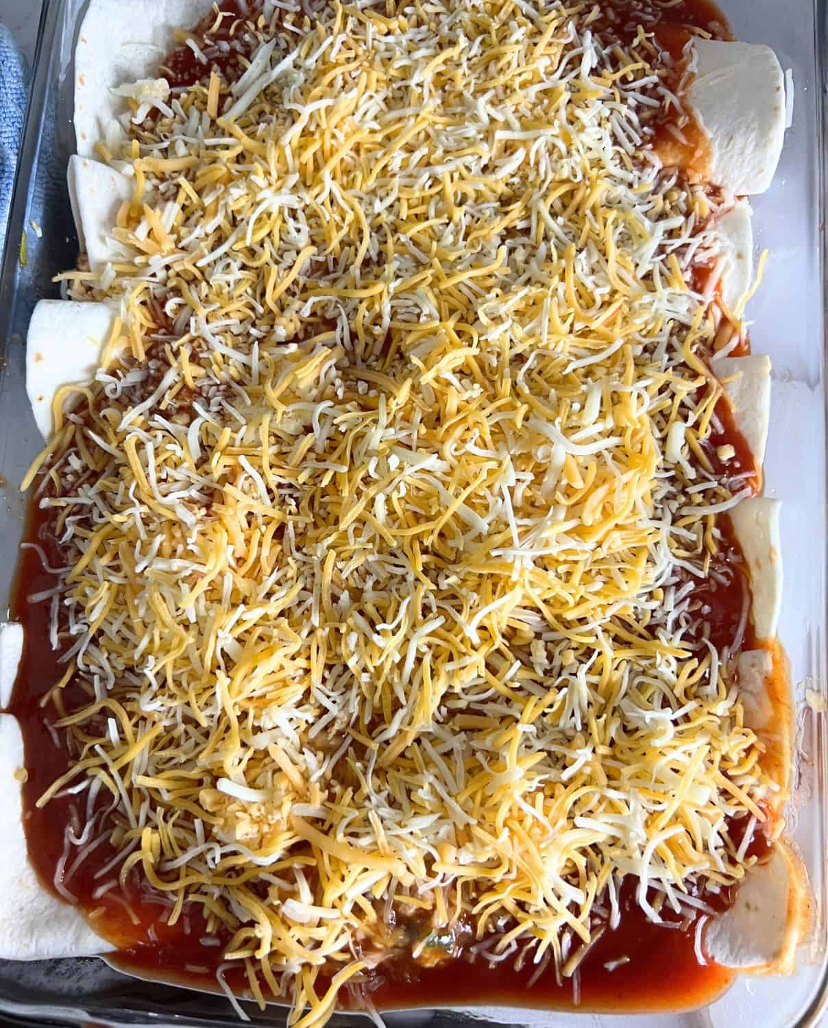 Prepared turkey enchiladas topped with sauce and some cheese ready for oven. 