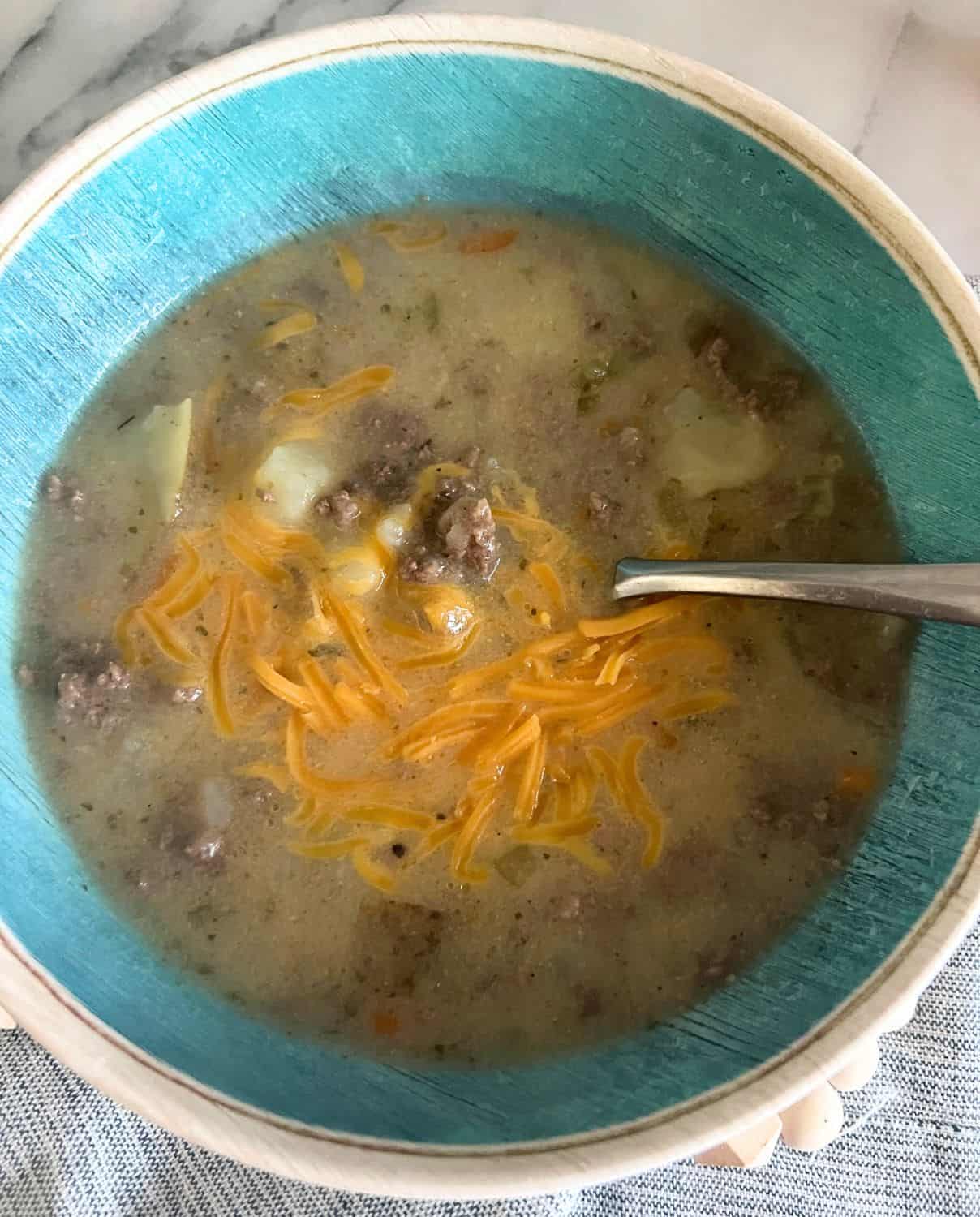 Cheeseburger soup topped with extra cheese in a blue bowl. 