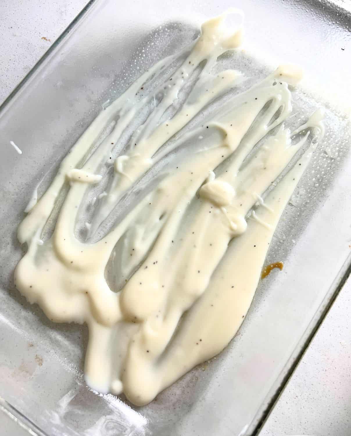 Alfredo sauce spread on the bottom of a clear casserole dish. 