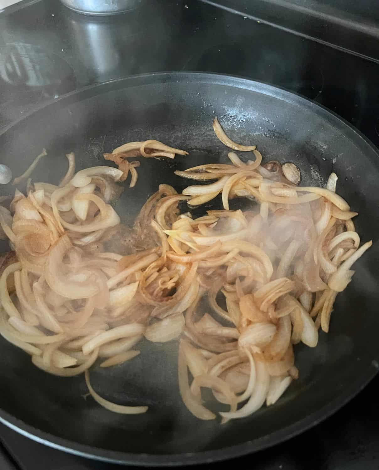 Onions, butter, and beef broth mixing in a pan.