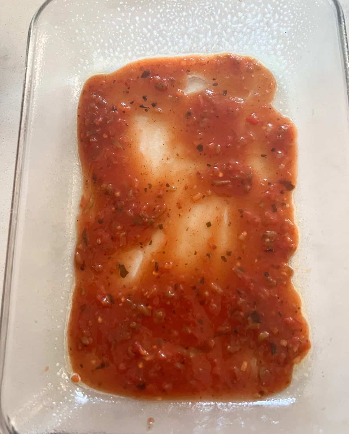 Enchilada sauce and salsa spread out on a casserole dish. 