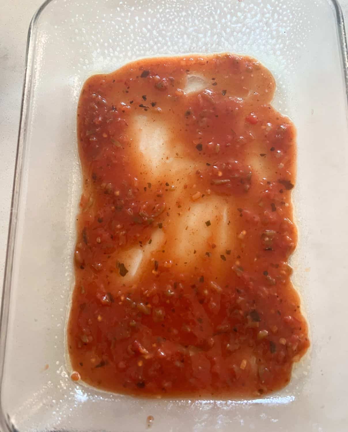 Enchilada sauce and salsa spread out on a casserole dish.
