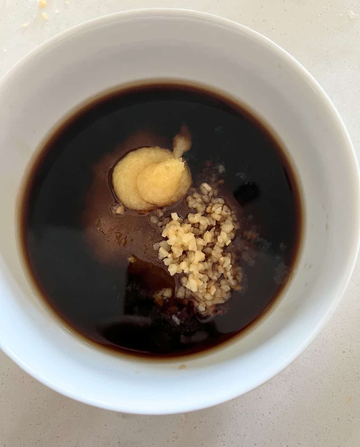 Ingredients for soy sauce, sugar, and garlic combined together in a small bowl. 