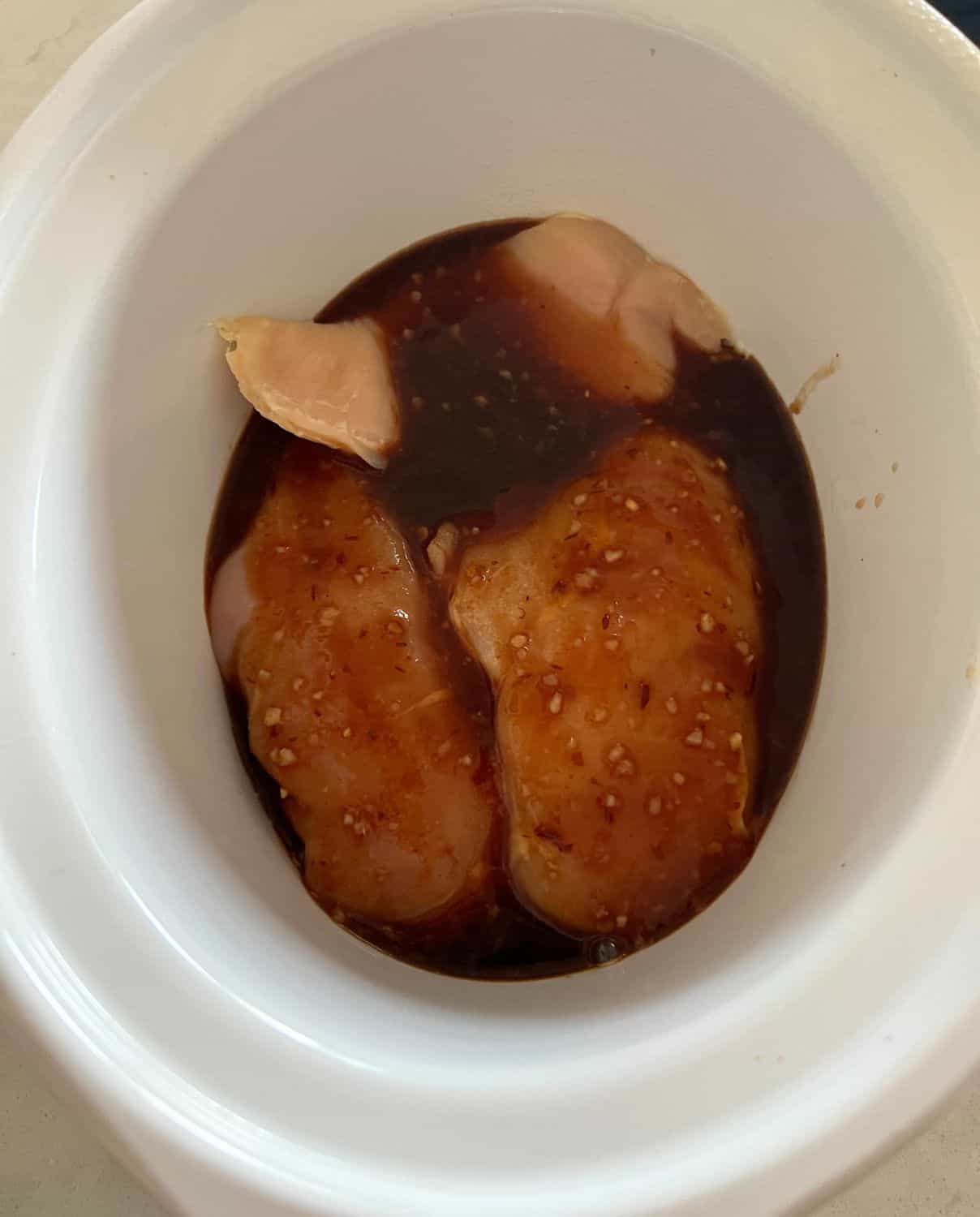 Chicken and sauce combined in a white slow cooker. 