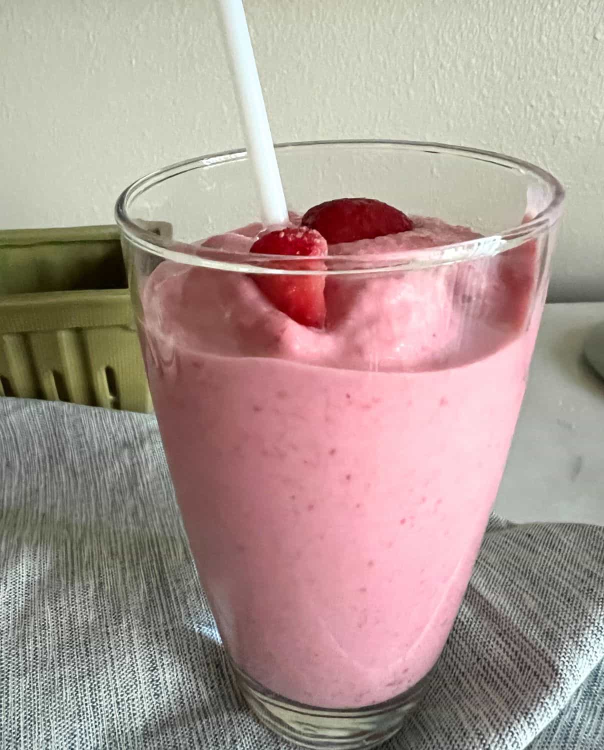 Strawberry cheesecake smoothie in a tall glass with a white straw. 