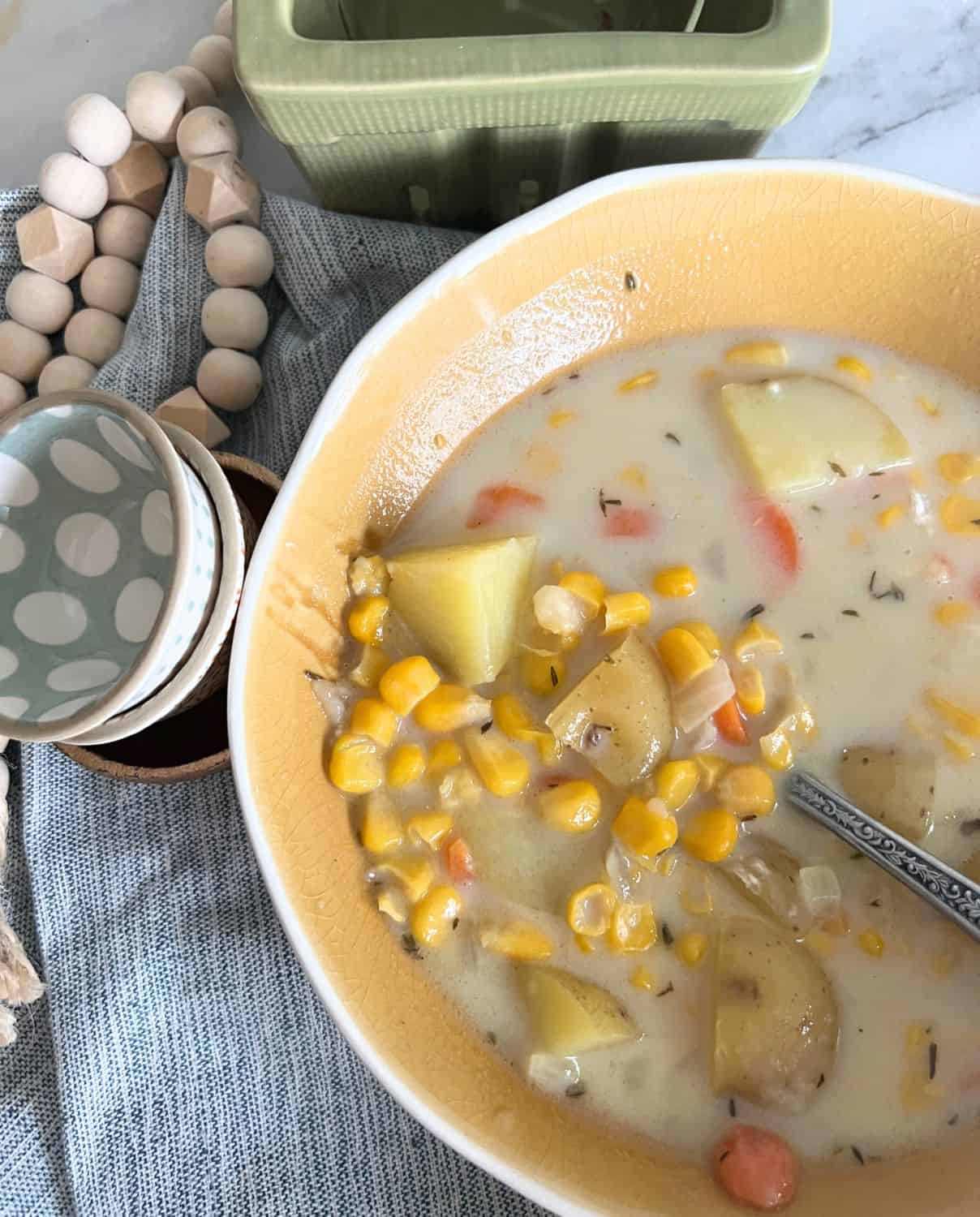 Corn chowder in a yellow bowl with a silver spoon. 