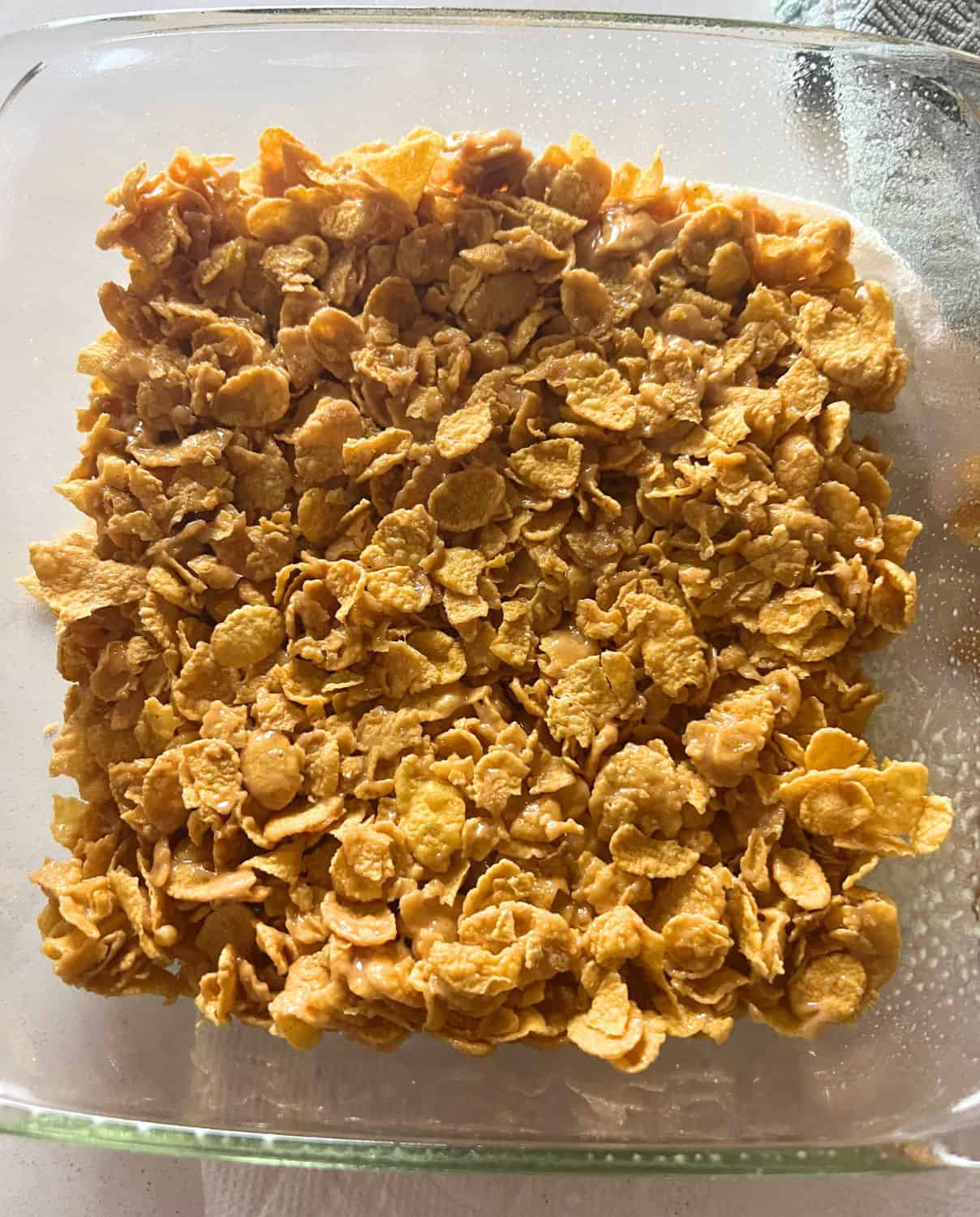 Cornflake peanut butter bars pressed into clear pan. 