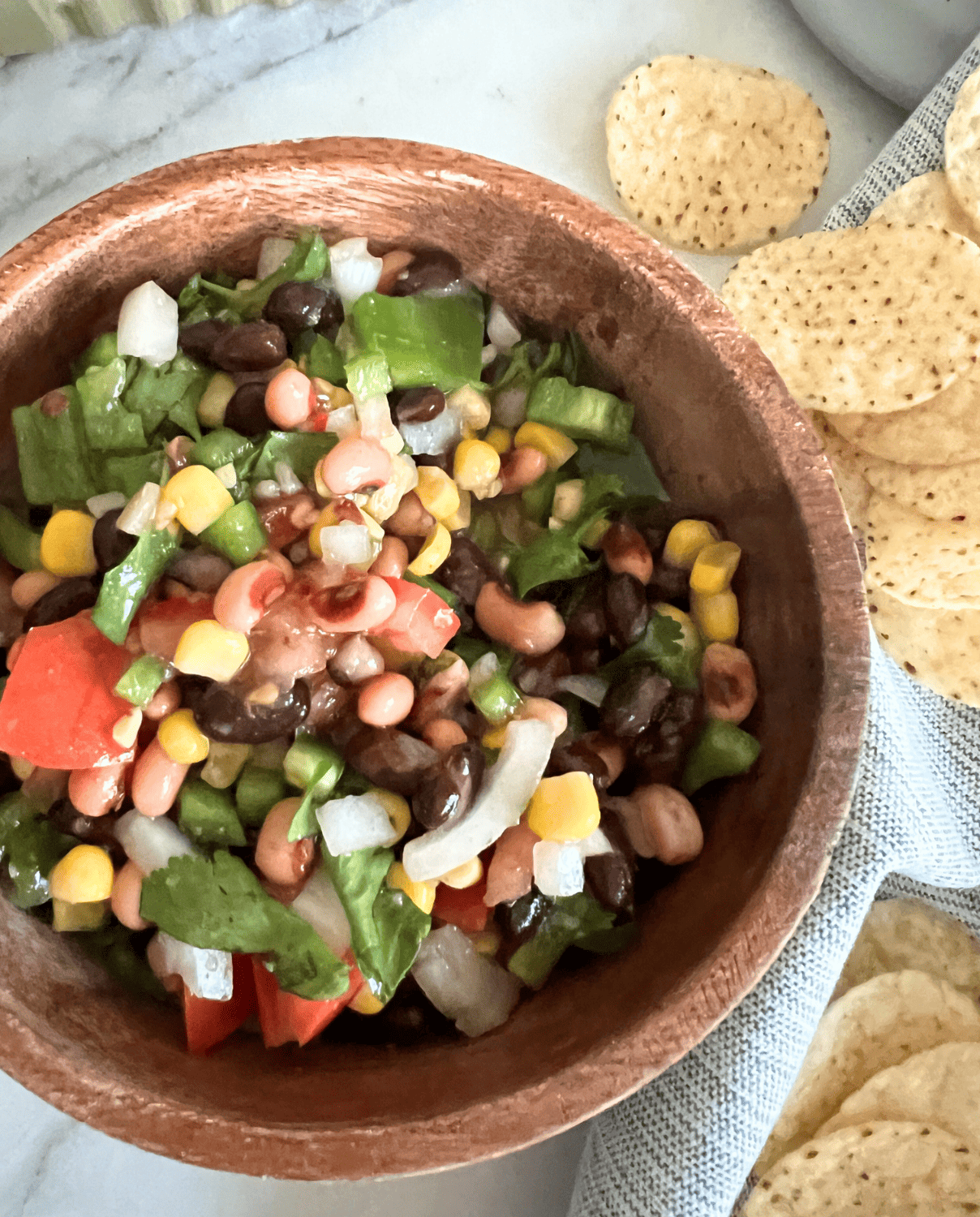 Cowboy caviar in a brown bowl next to some tortilla chips. 
