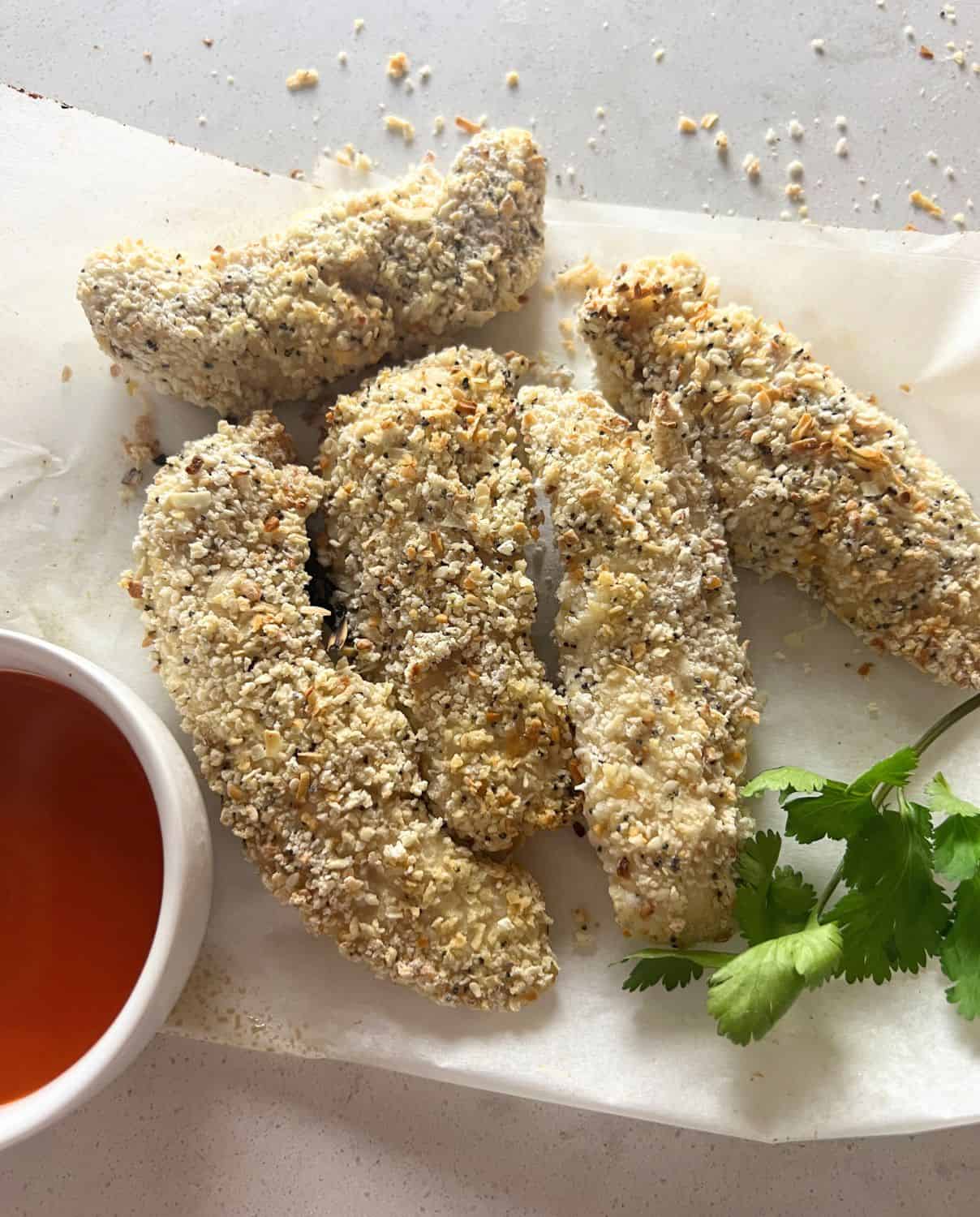 Air fryer chicken tenders on white parchment paper next to a white bowl with buffalo wing sauce. 