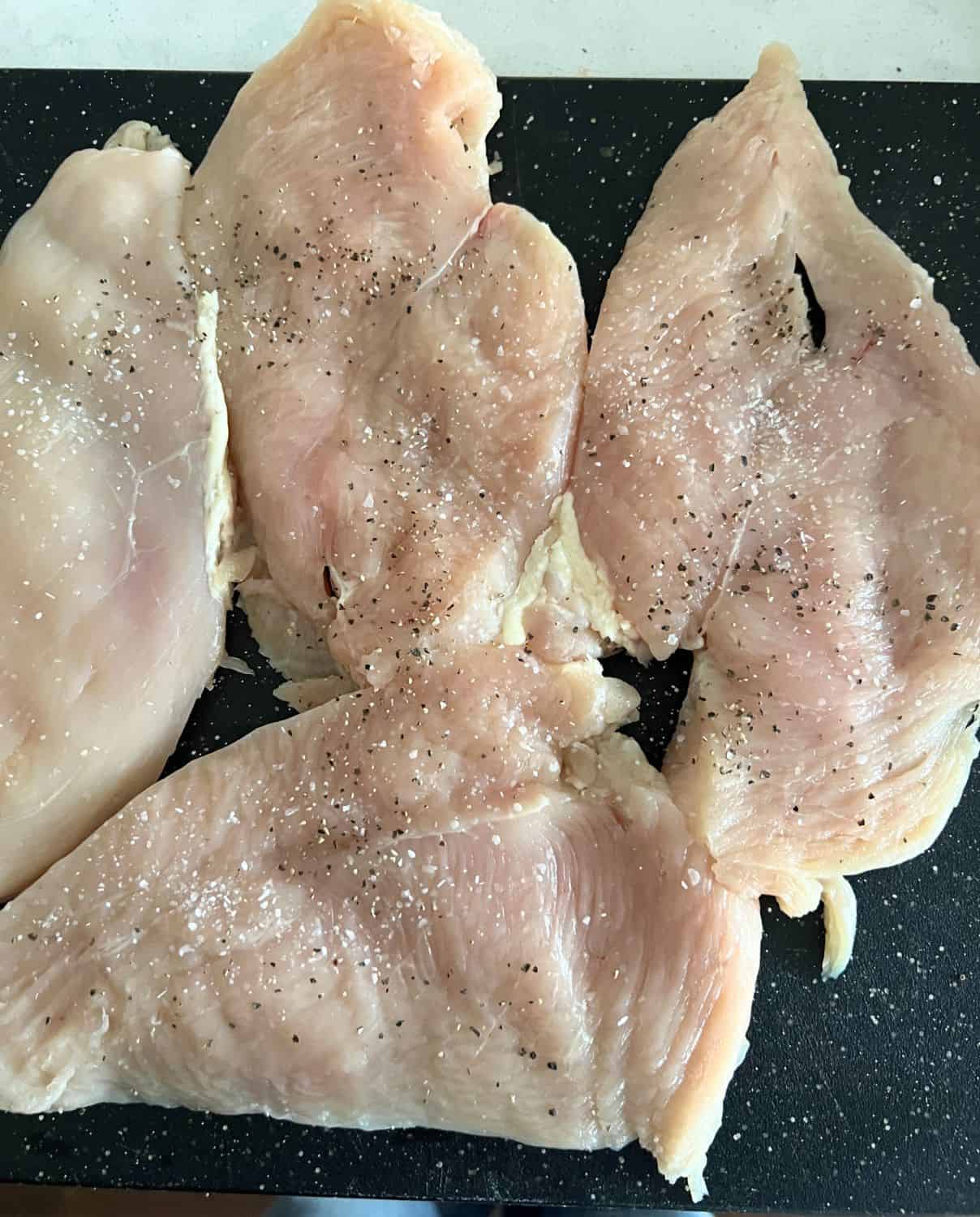 Pounded thin chicken breasts on a cutting board seasoned with salt and pepper. 
