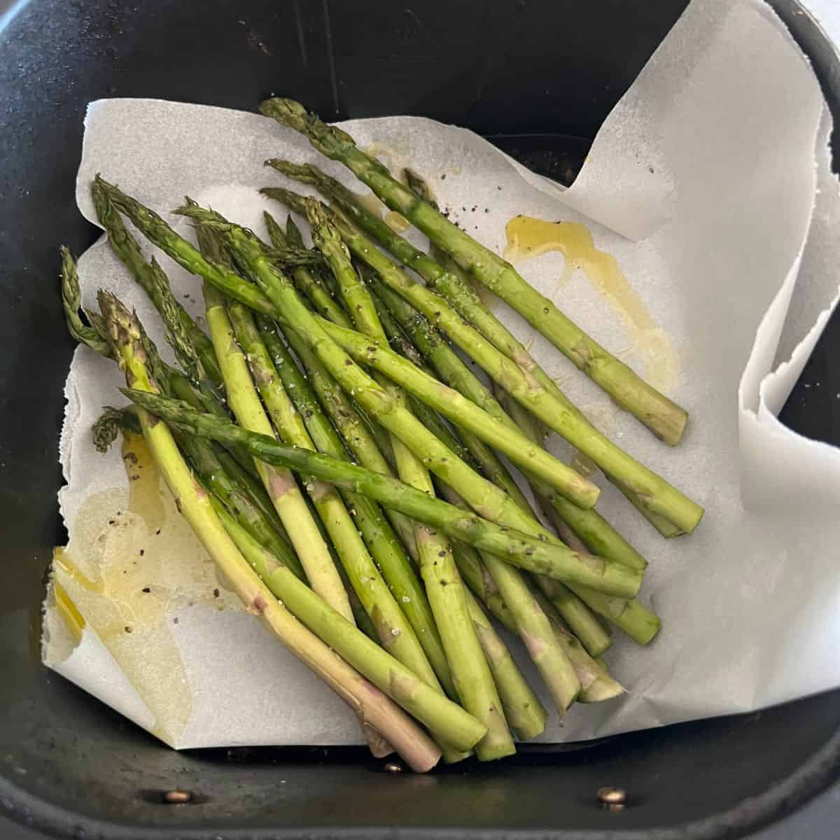 Asparagus in air fryer basket seasoned with salt and pepper. 