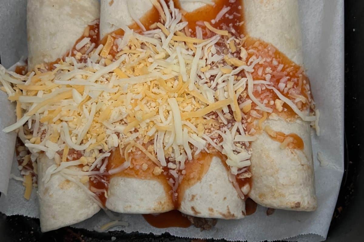 Cheese enchilada sauce on top of enchiladas in an air fryer basket. 