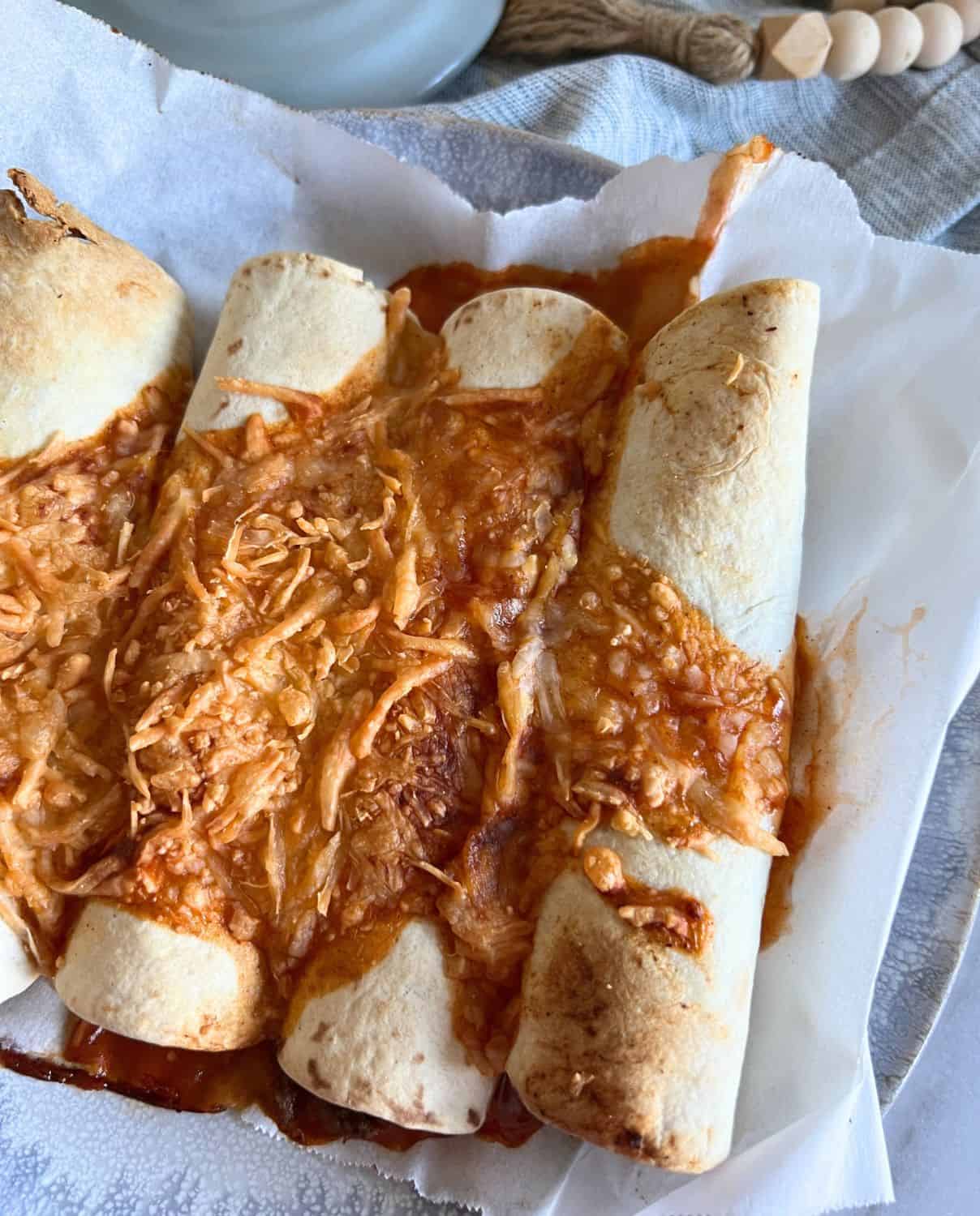 Air fryer beef enchiladas served on a blue plated and topped with cheese and enchilada sauce. 