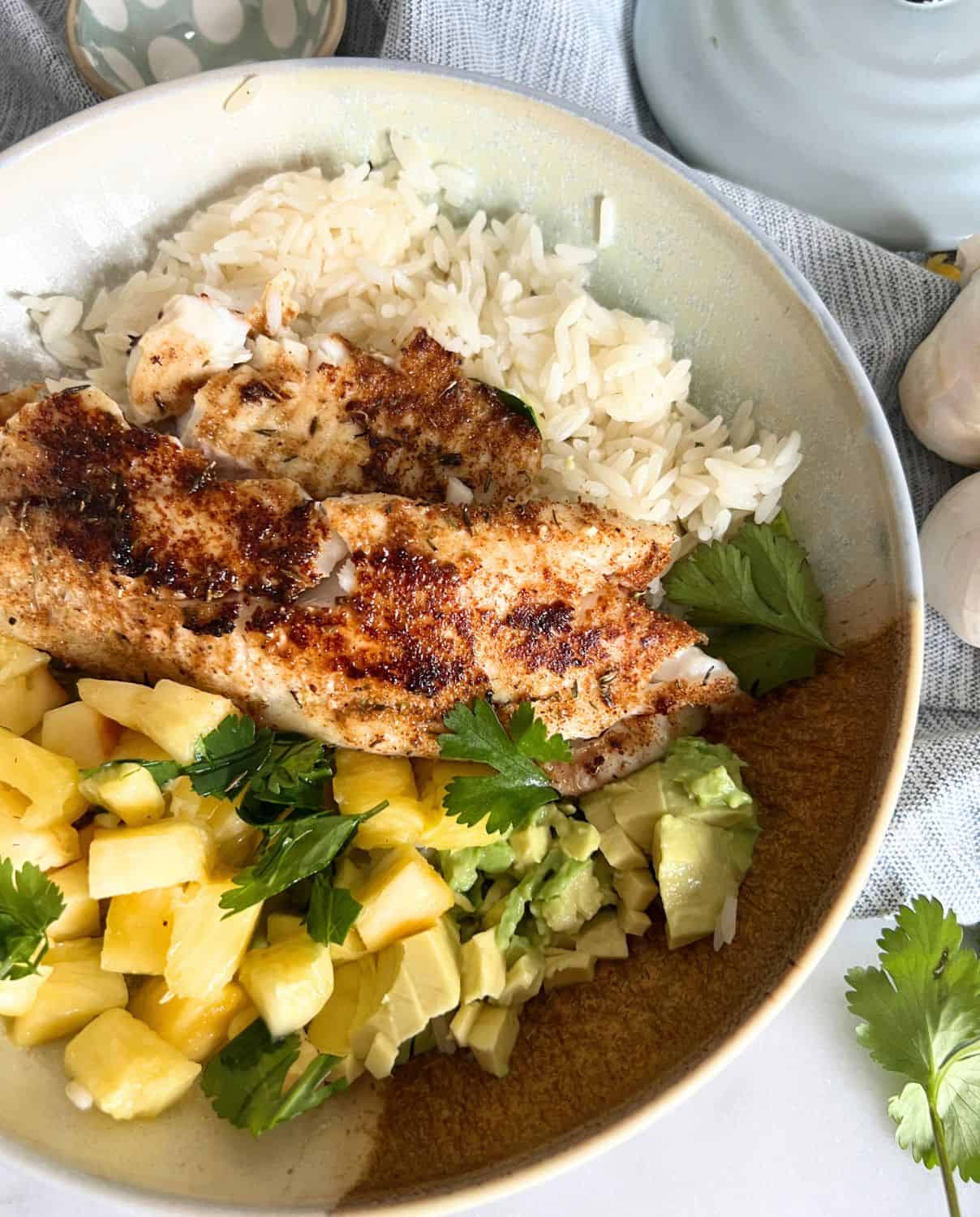 Blackened tilapia on top of rice served with some fresh pineapple and guacamole. 