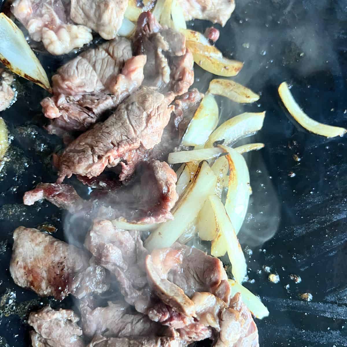 Steak and onions cooking on a Blackstone griddle. 