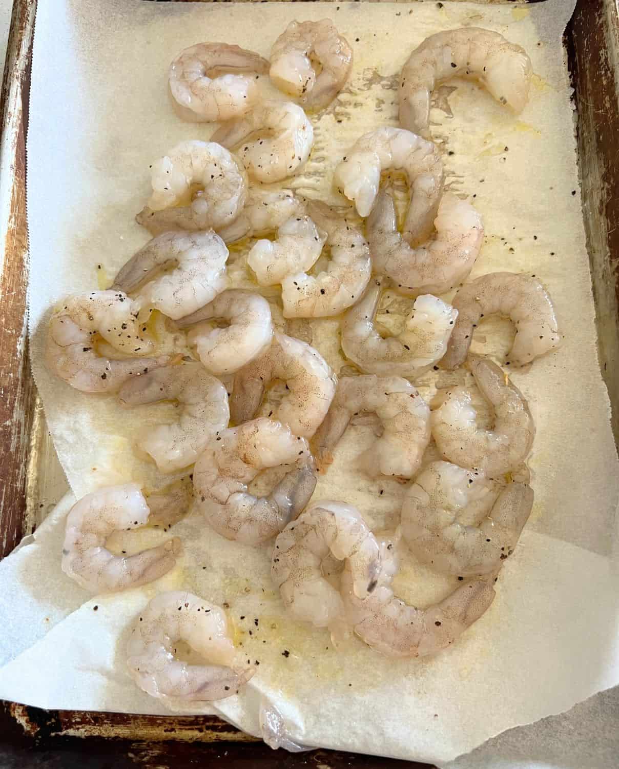Raw shrimp seasoned with salt and pepper on a lined baking sheet. 