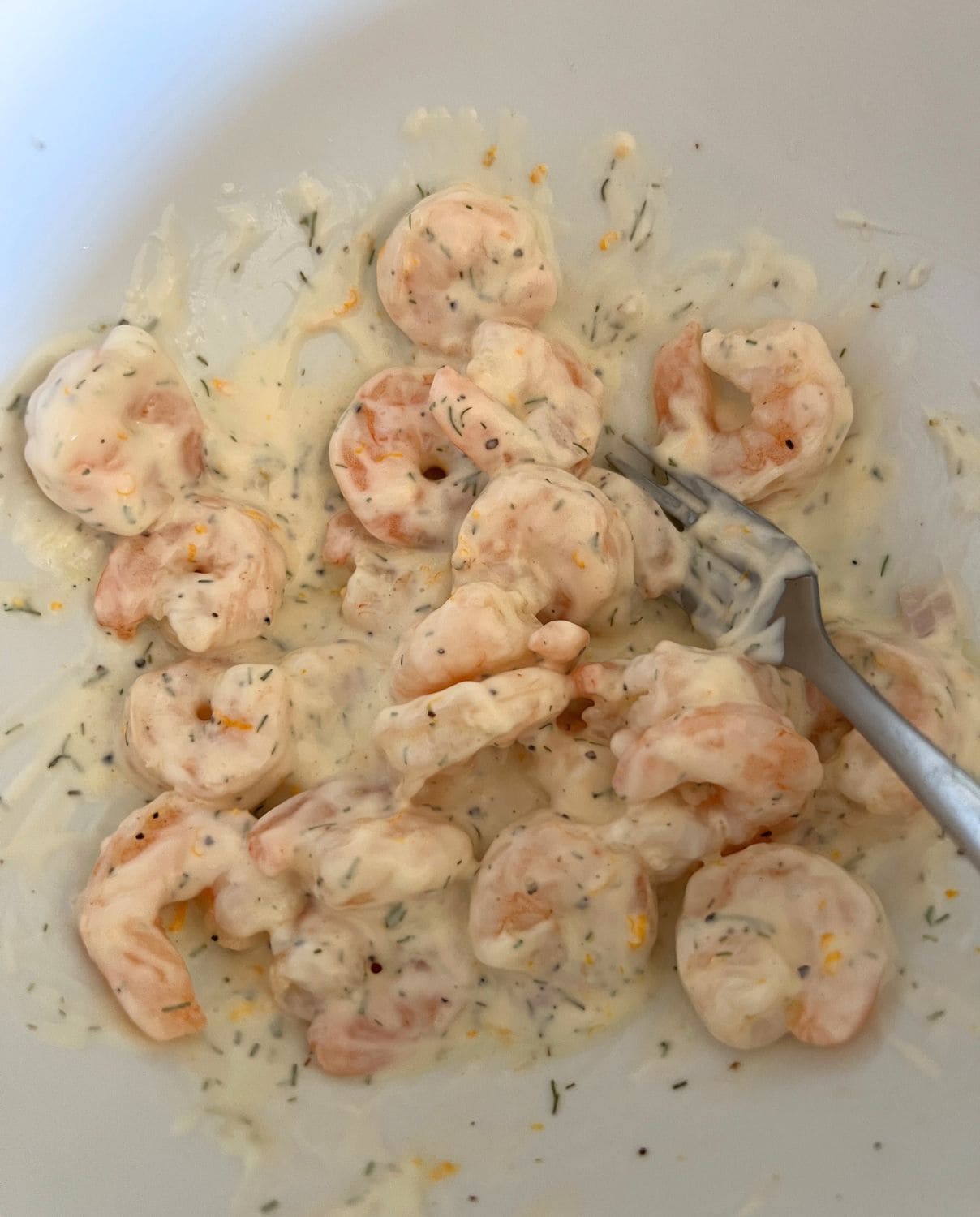 Cooked shrimp combined with dressing in a bowl. 