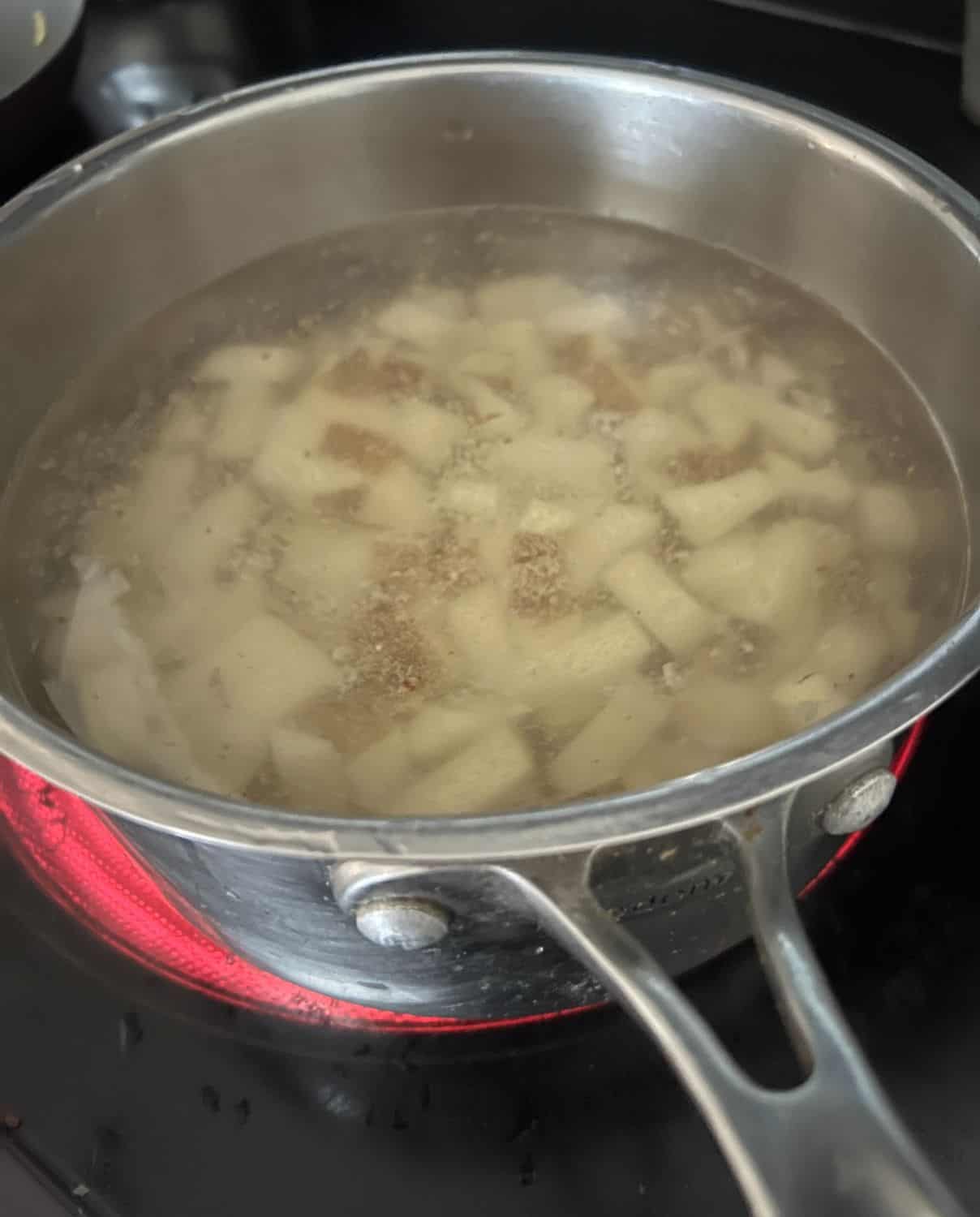 Cut up potatoes boiling on a stove top. 