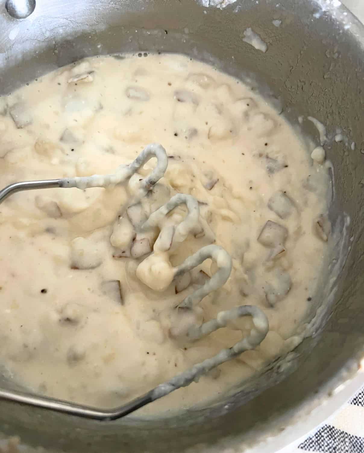 Mashed potatoes with a potato masher in a pot. 
