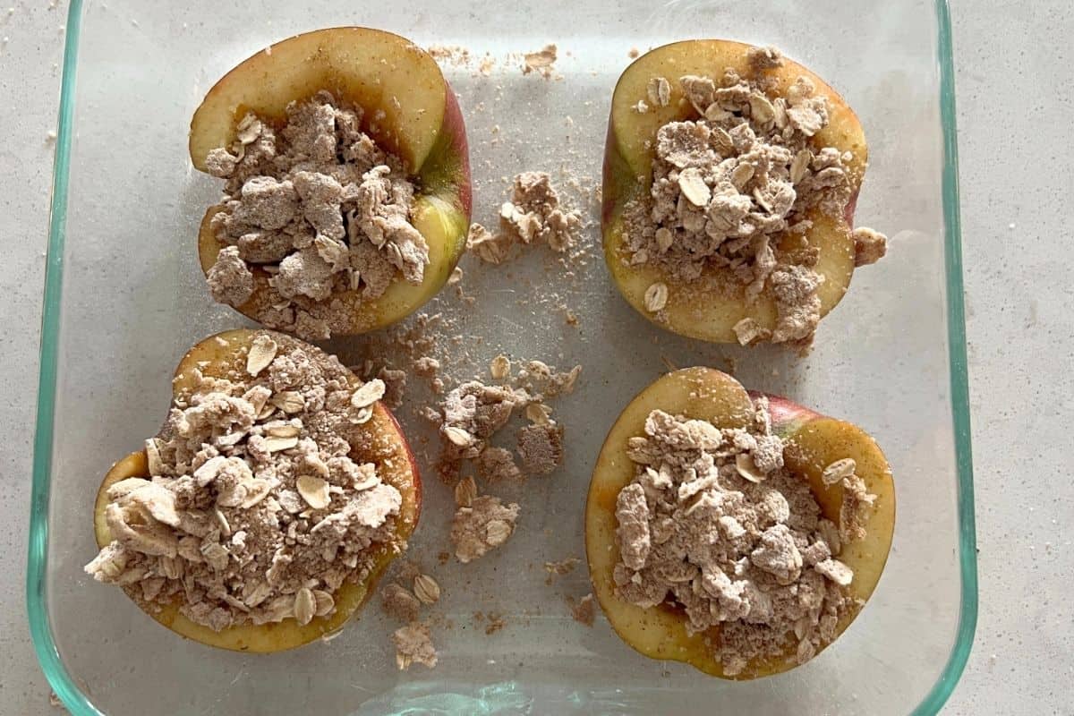 Apples topped with oat mixture in a clear baking dish. 