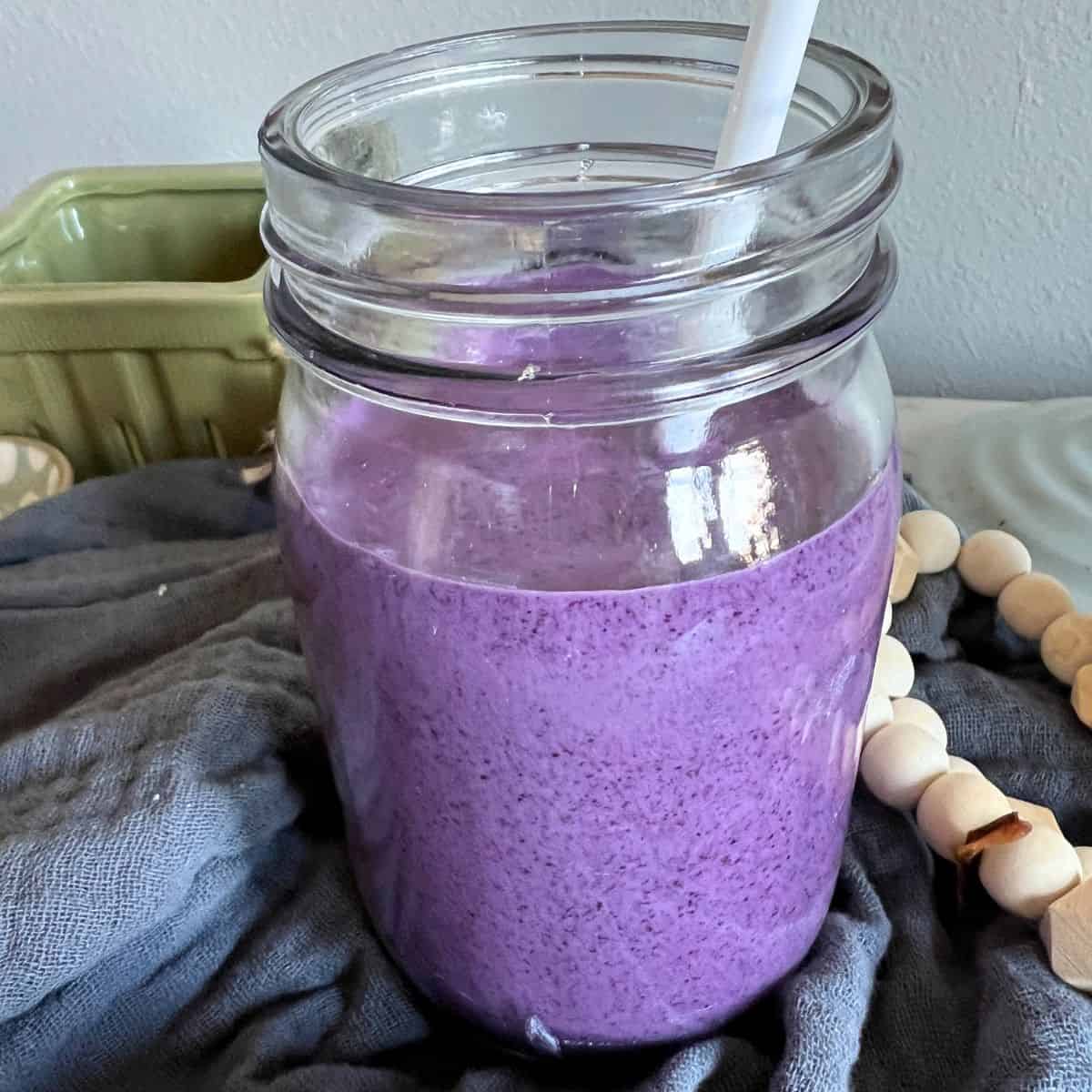 Blueberry smoothie in a glass jar with a straw. 