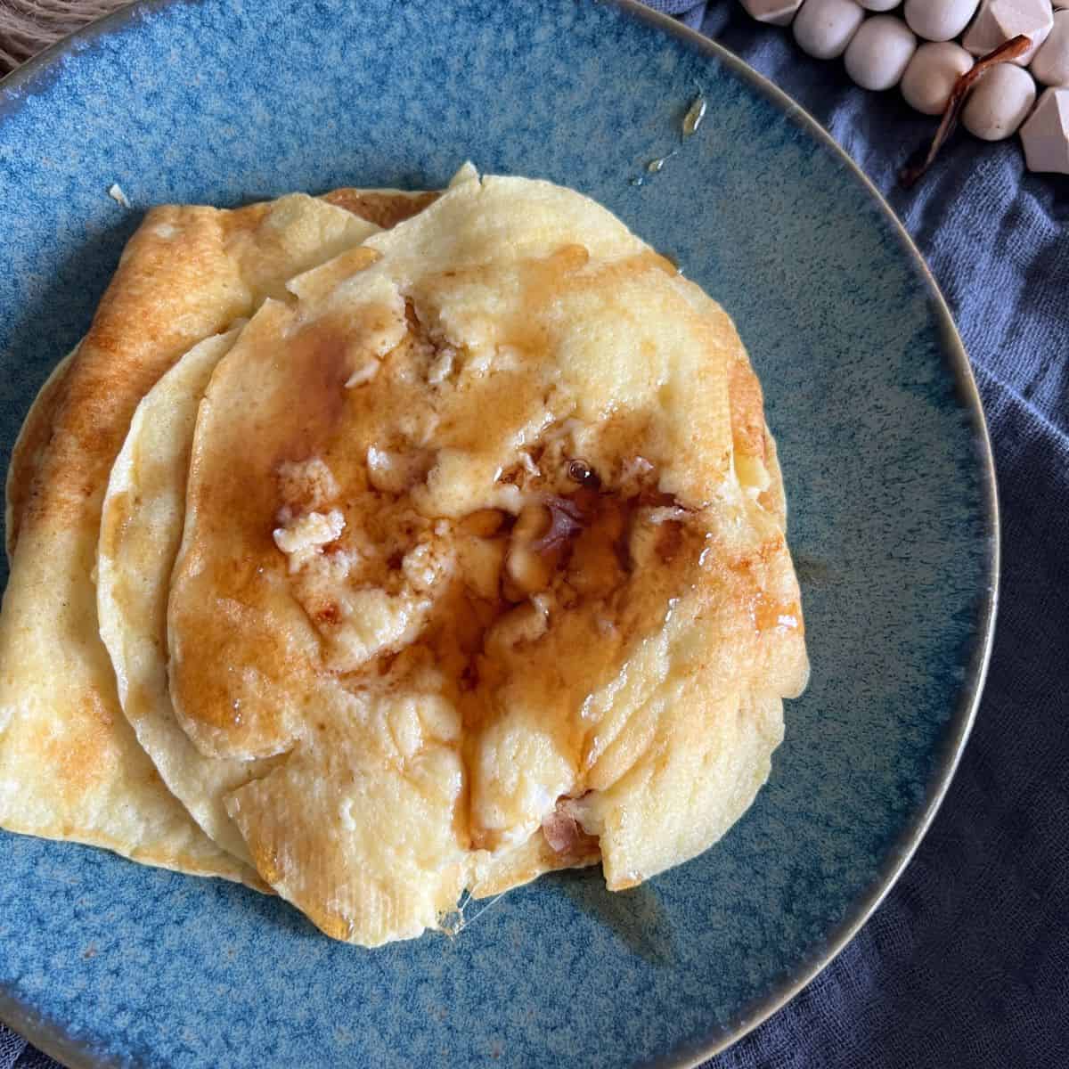 Cottage cheese pancakes topped with maple syrup on a blue plate. 