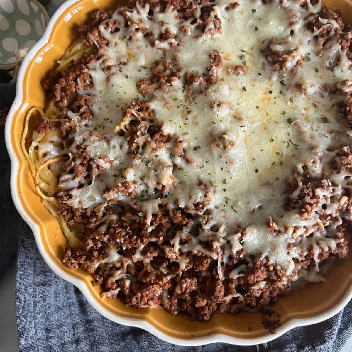 Spaghetti pie topped with melted cheese in a an orange pie dish. 