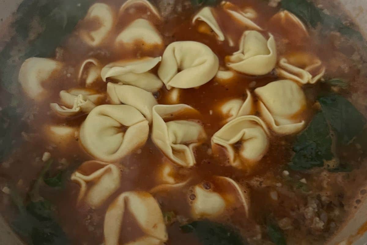 Tortellini and spinach simmering in a pot.