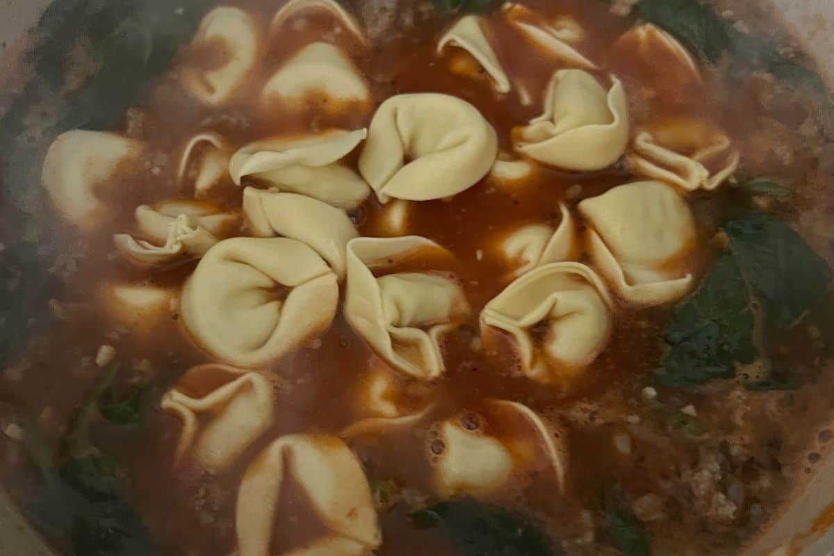 Tortellini and spinach simmering in a pot. 