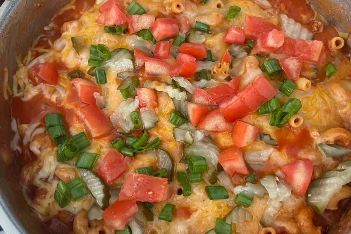 Cheeseburger pasta topped with tomatoes, onions, and pickles. 