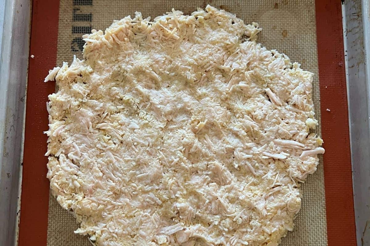 Chicken crust pizza layed out in a round circle on a baking sheet. 