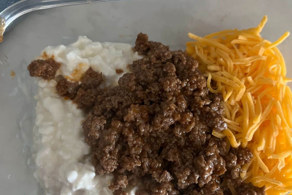 Cheese, ground beef, and shredded cheese in a pyrex bowl. 