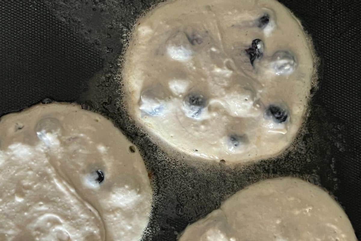 Blueberry pancakes cooking on a griddle. 