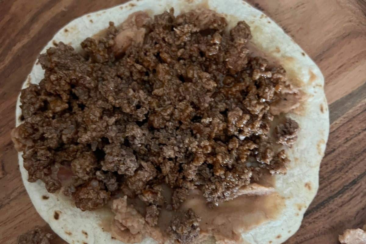Refried beans on top of a tortilla and ground beef. 