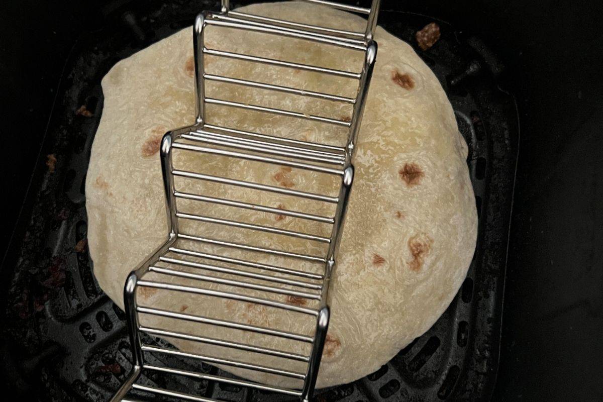 Tortilla mexican pizza in an air fryer basket with a trivet on top. 