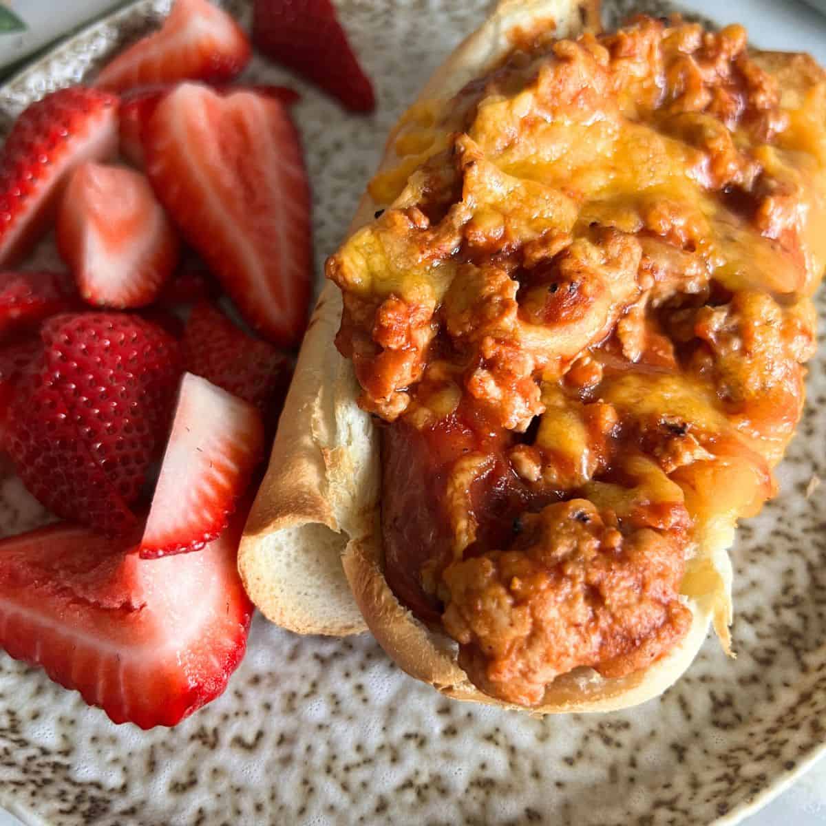 Air fryer hot dogs topped with chili and cheese next to strawberries. 