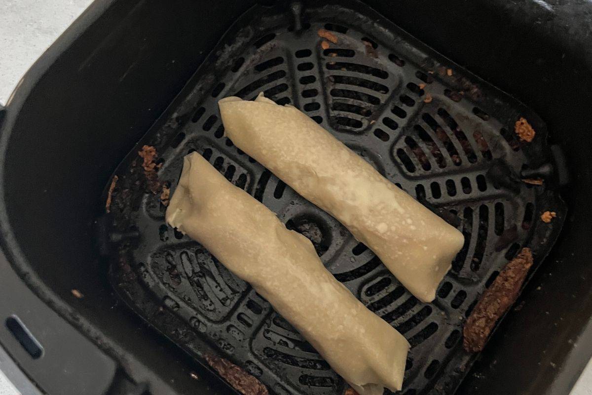 Rolled up pizza egg rolls in air fryer basket. 