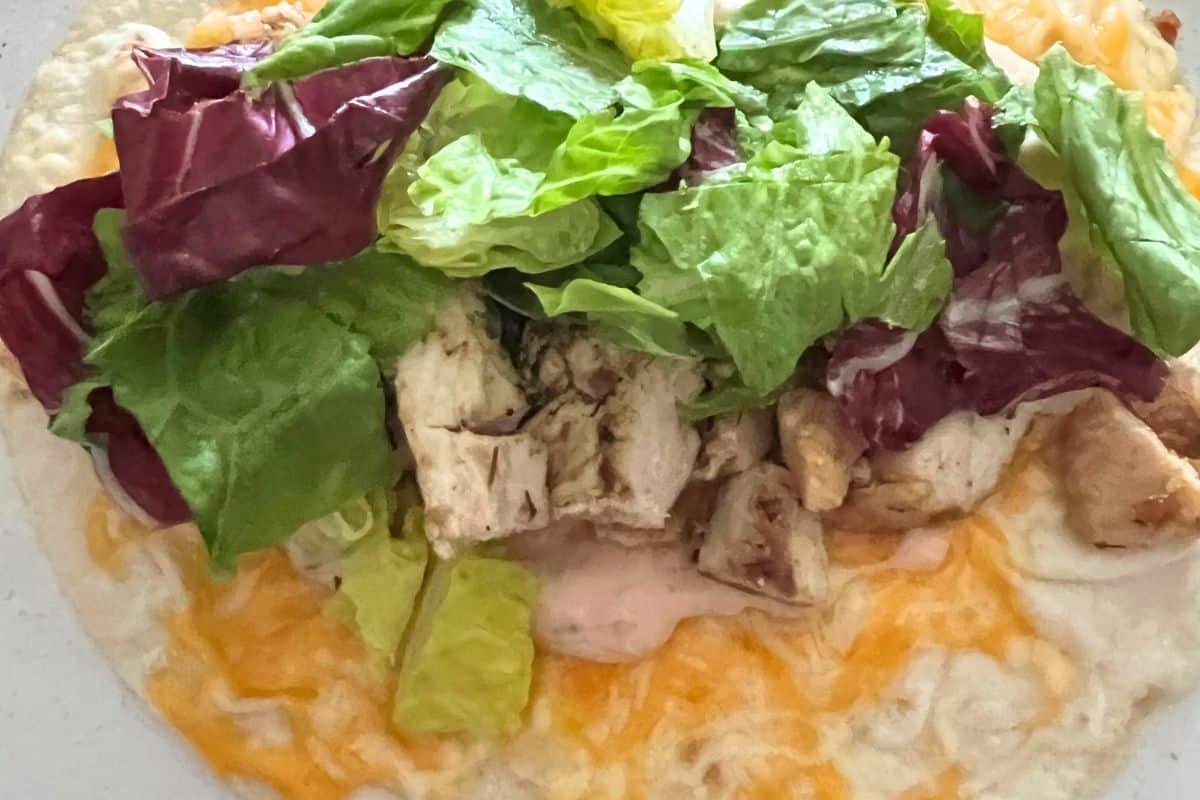 Lettuce, chicken, and sauce on top of a cheesy tortilla. 