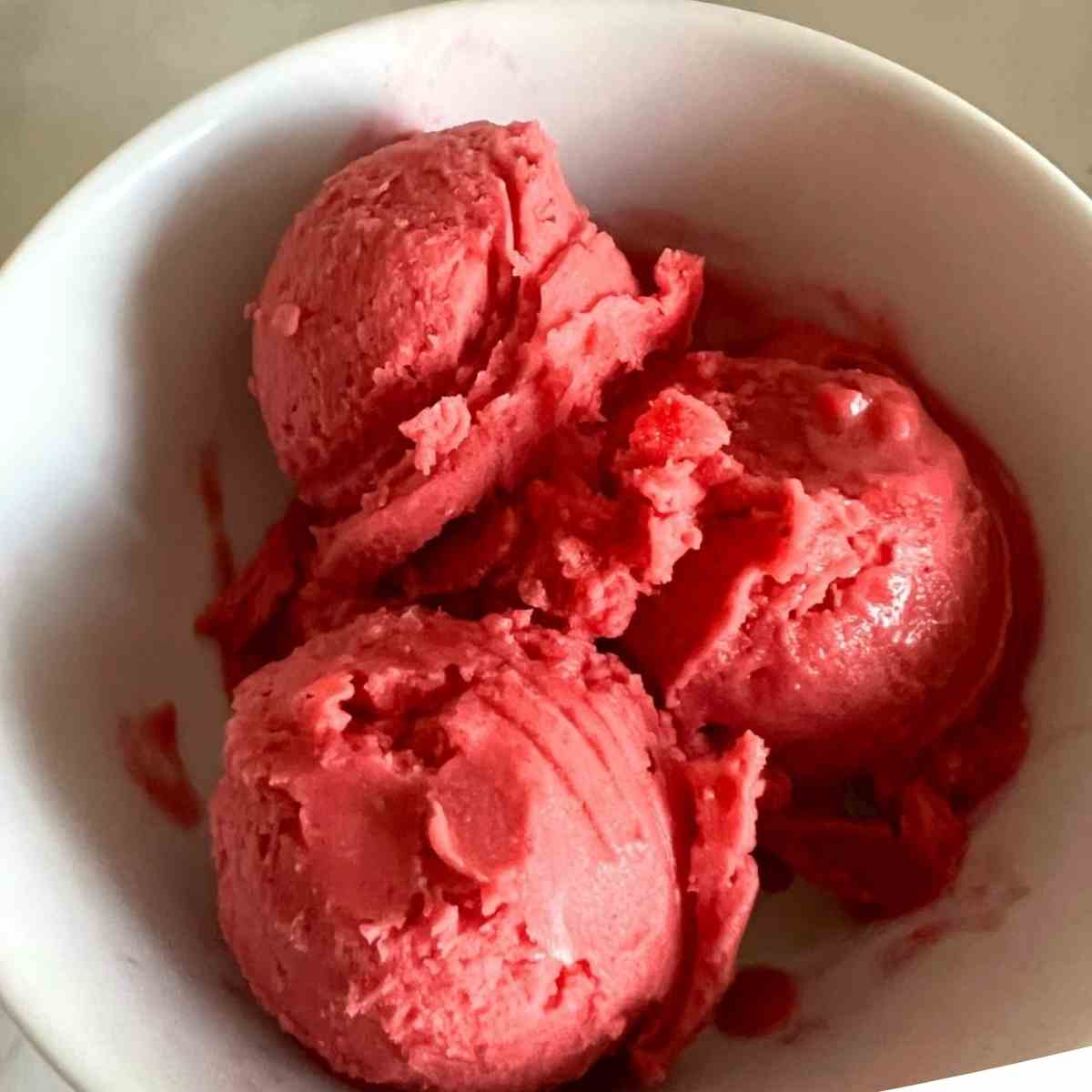 3 scoops of Ninja creami raspberry sorbet in a white bowl.