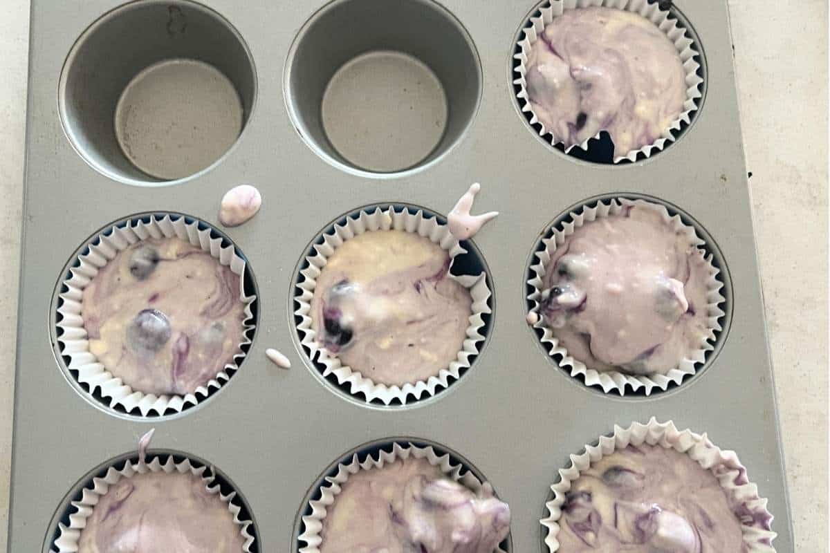 Blueberry muffin batter added to muffin tin cup.