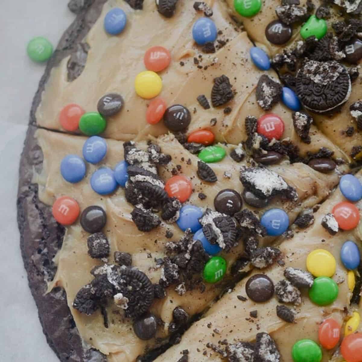 Peanut butter brownie pizza topped with peanut butter frosting and candy pieces.