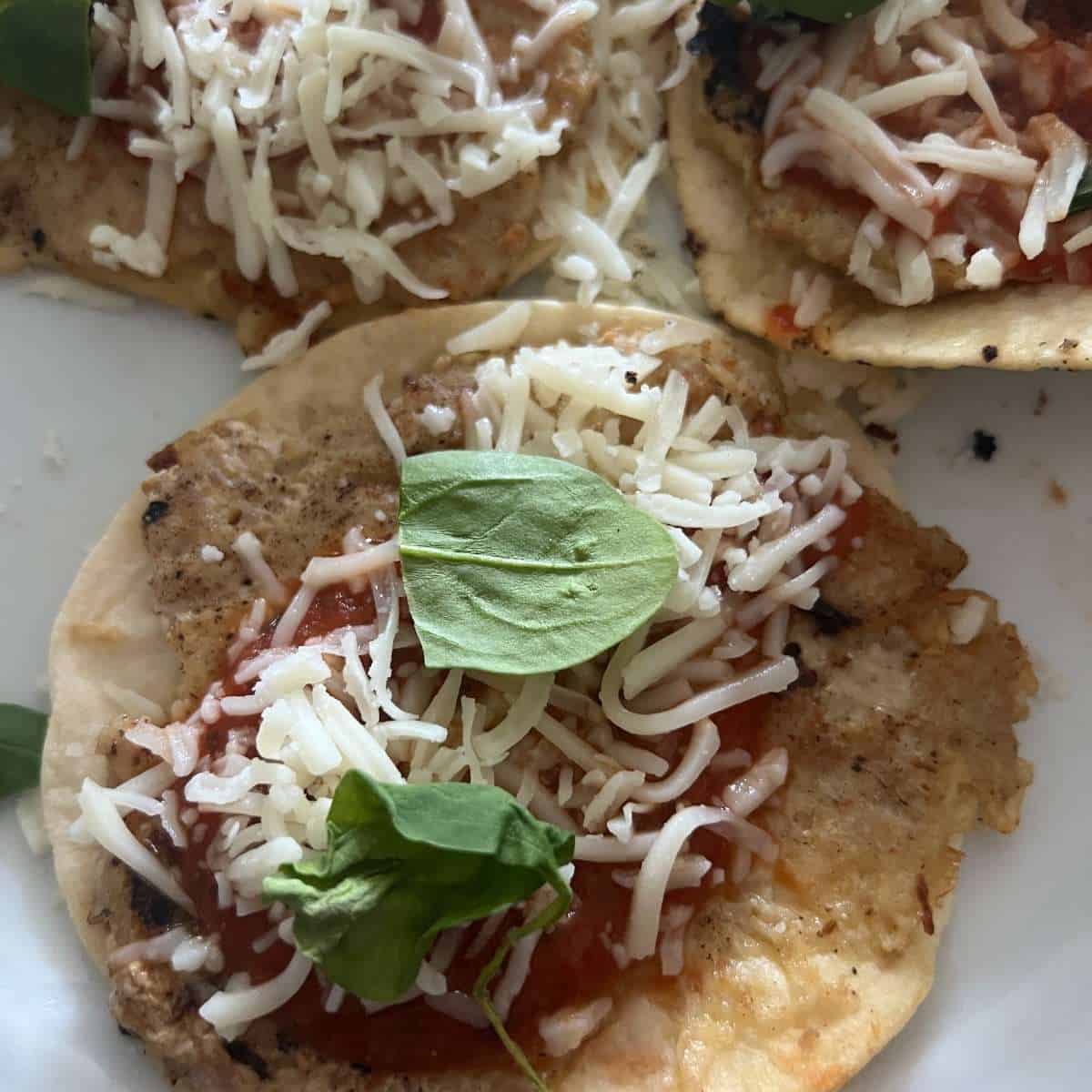 Chicken parmesan tacos topped with cheese, tomato sauce, and basil.